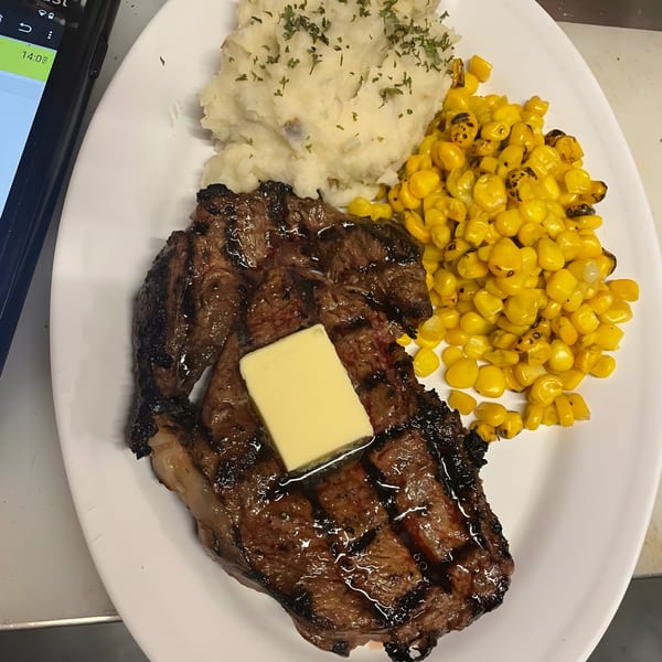 Grilled steak with a pat of butter, mashed potatoes, and corn on a white plate.