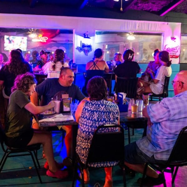 Patrons enjoying food and drinks at tables in a lively, neon-lit Goofy's Grill bar-and-grill.