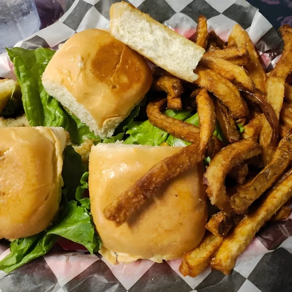 Three sliders with lettuce and sauce, served with a side of crispy french fries in a checkered basket.