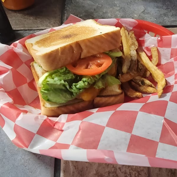 A Goofy's Grill sandwich with lettuce and tomato, served with fries in a red checkered basket.