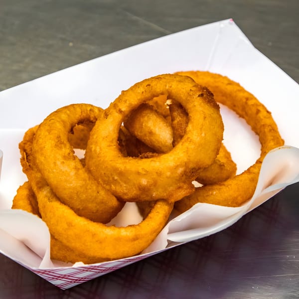 Golden-brown onion rings from Goofy's Grill, served in a white paper tray with red checkered trim.