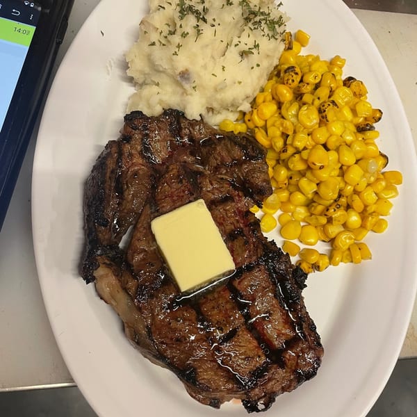 Grilled steak with a pat of butter, mashed potatoes, and corn on a white plate.