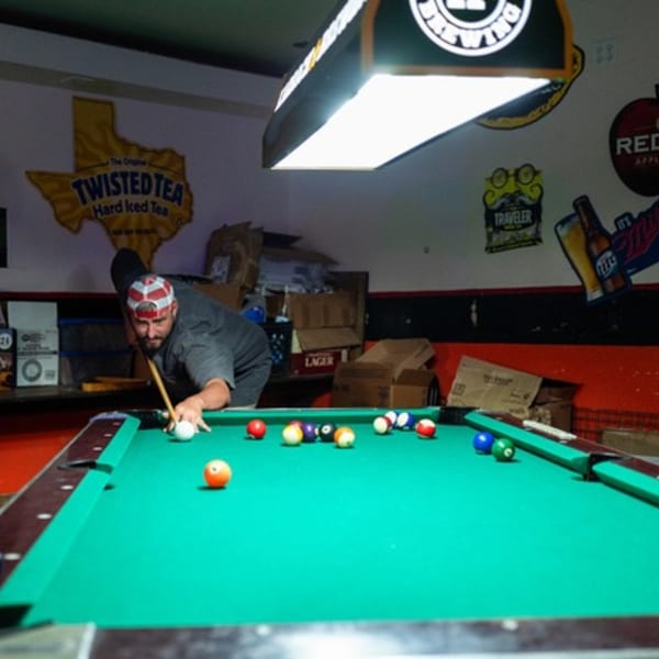 Man playing pool at Goofy's Grill, aiming a shot on a green billiard table.
