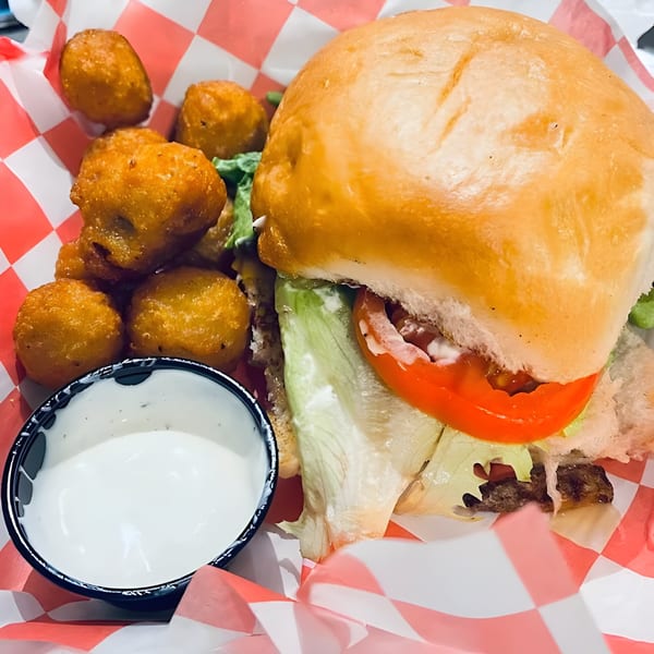 Goofy's Grill burger with lettuce, tomato, and a side of fried cheese curds and dipping sauce.
